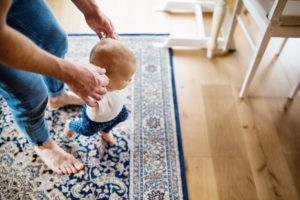 father helping toddler walk on a blue patterned rug